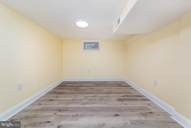 finished basement with baseboards, visible vents, and wood finished floors