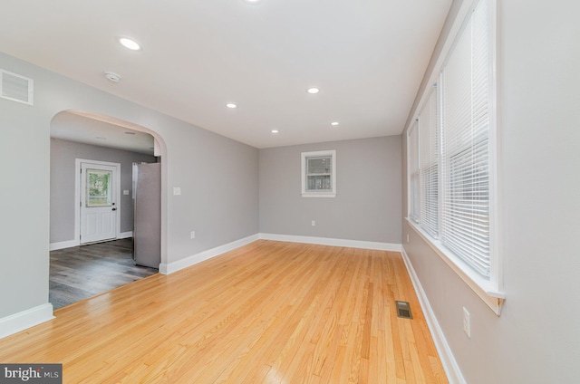 spare room with arched walkways, wood finished floors, visible vents, and baseboards