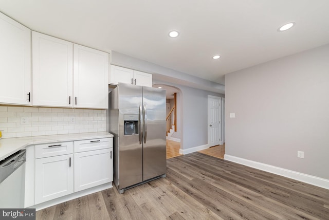 kitchen with arched walkways, stainless steel appliances, white cabinets, light wood-style floors, and backsplash