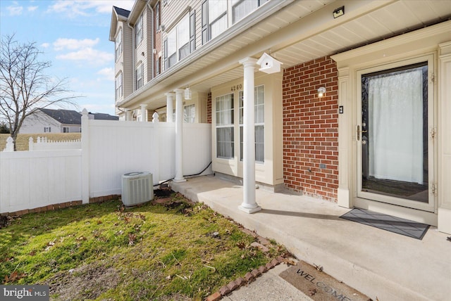 doorway to property featuring central AC unit, fence, and brick siding