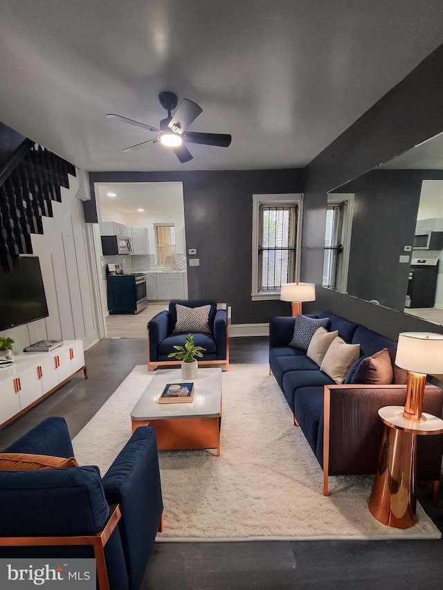 living room with baseboards, stairs, and ceiling fan