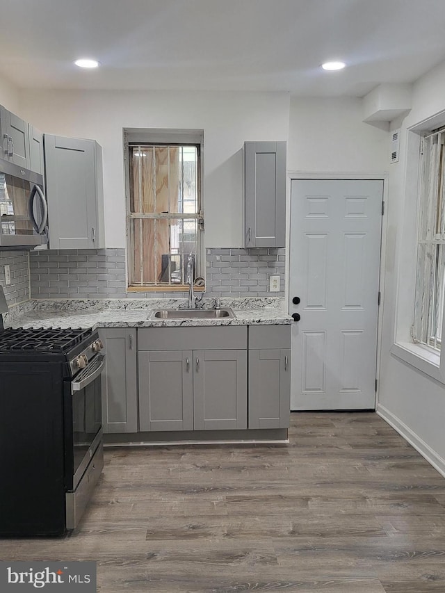 kitchen featuring light stone counters, appliances with stainless steel finishes, wood finished floors, gray cabinets, and a sink