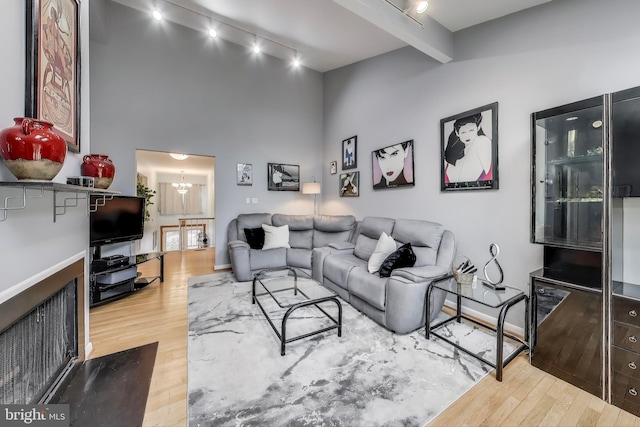 living room featuring baseboards, wood finished floors, rail lighting, beam ceiling, and a notable chandelier