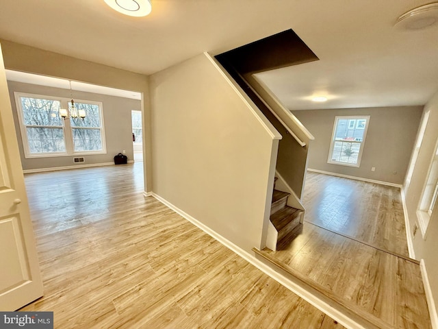 corridor with visible vents, wood finished floors, stairway, baseboards, and a chandelier