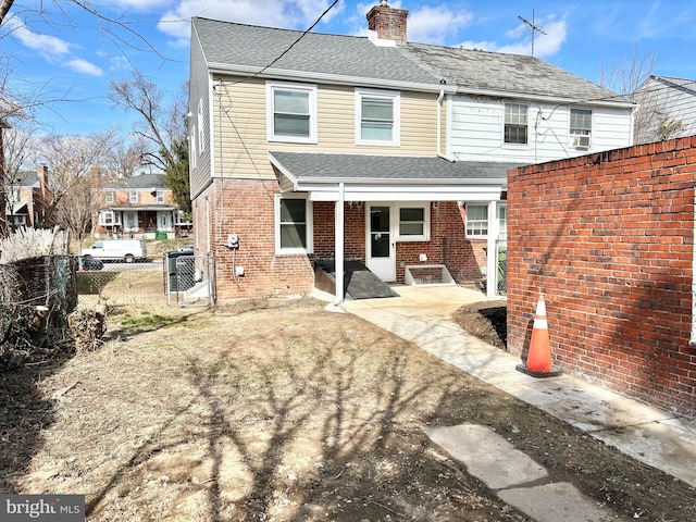 back of house featuring brick siding, fence, a chimney, and roof with shingles