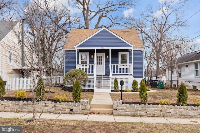 bungalow with covered porch, roof with shingles, and fence