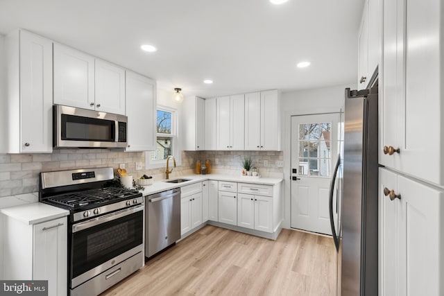 kitchen with light wood finished floors, decorative backsplash, appliances with stainless steel finishes, white cabinetry, and a sink