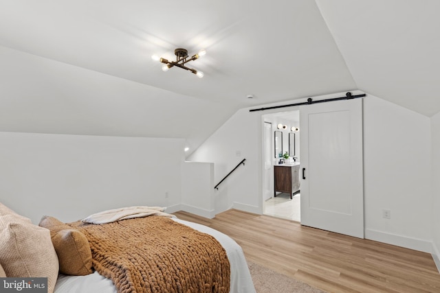 bedroom with light wood-style flooring, baseboards, vaulted ceiling, and a barn door