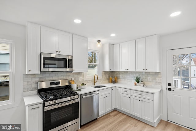 kitchen with light wood-style flooring, decorative backsplash, appliances with stainless steel finishes, white cabinetry, and a sink