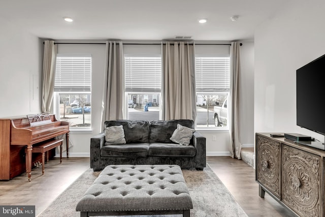 living room with light wood-type flooring, a wealth of natural light, visible vents, and baseboards