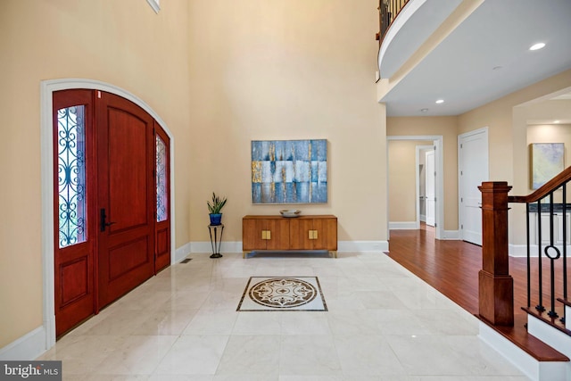 entryway with arched walkways, a towering ceiling, baseboards, and stairs