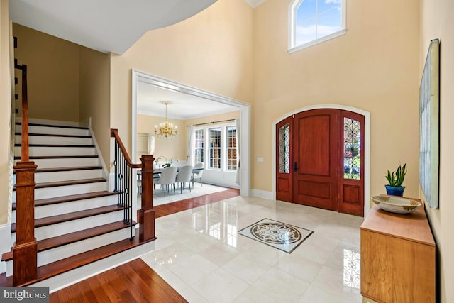 entryway with baseboards, stairway, ornamental molding, an inviting chandelier, and a high ceiling