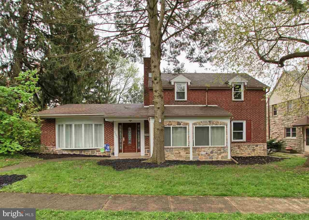 traditional-style home featuring stone siding, a front lawn, and a chimney