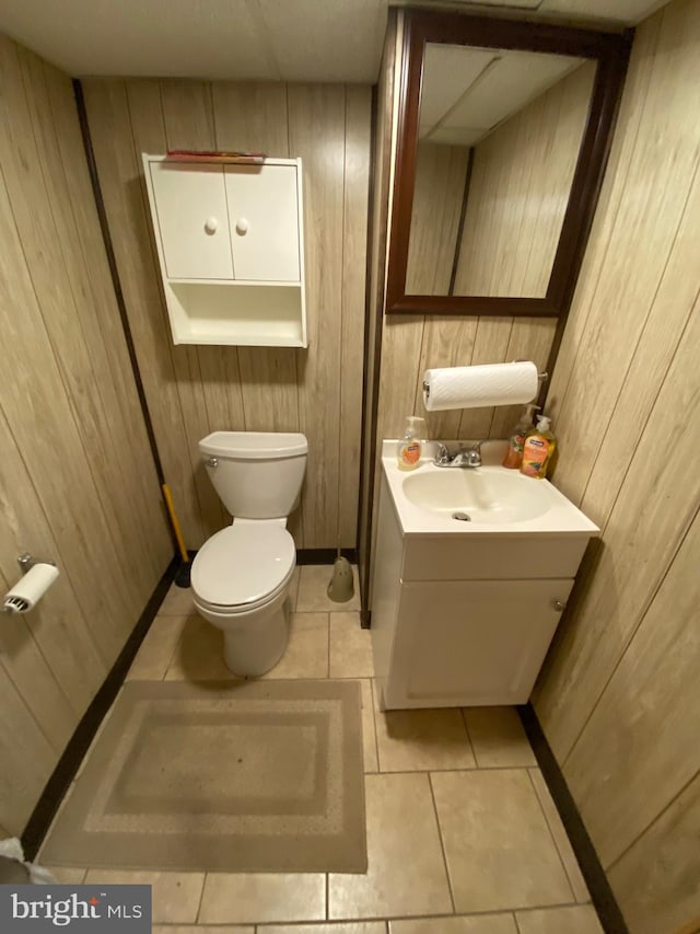 half bathroom with wood walls, toilet, vanity, and tile patterned floors