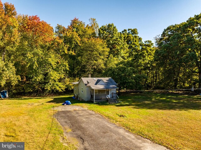 view of front facade with covered porch, aphalt driveway, a chimney, and a front yard