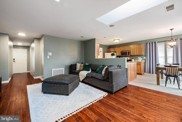 living area with a skylight, baseboards, visible vents, and wood finished floors