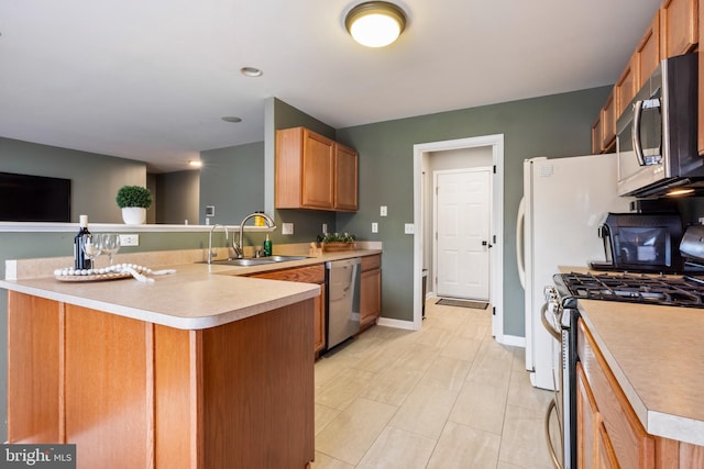 kitchen with light countertops, appliances with stainless steel finishes, a peninsula, and a sink