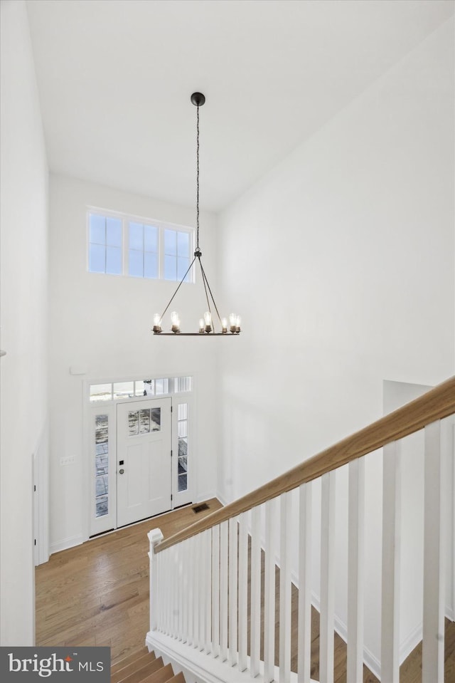 foyer featuring stairway, an inviting chandelier, a towering ceiling, and wood finished floors