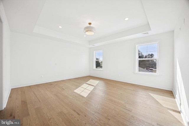 empty room featuring baseboards, light wood-style floors, a raised ceiling, and visible vents