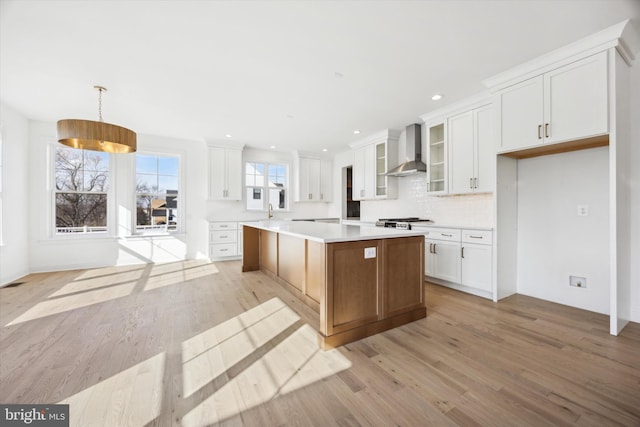 kitchen with light countertops, a center island, white cabinets, and wall chimney exhaust hood