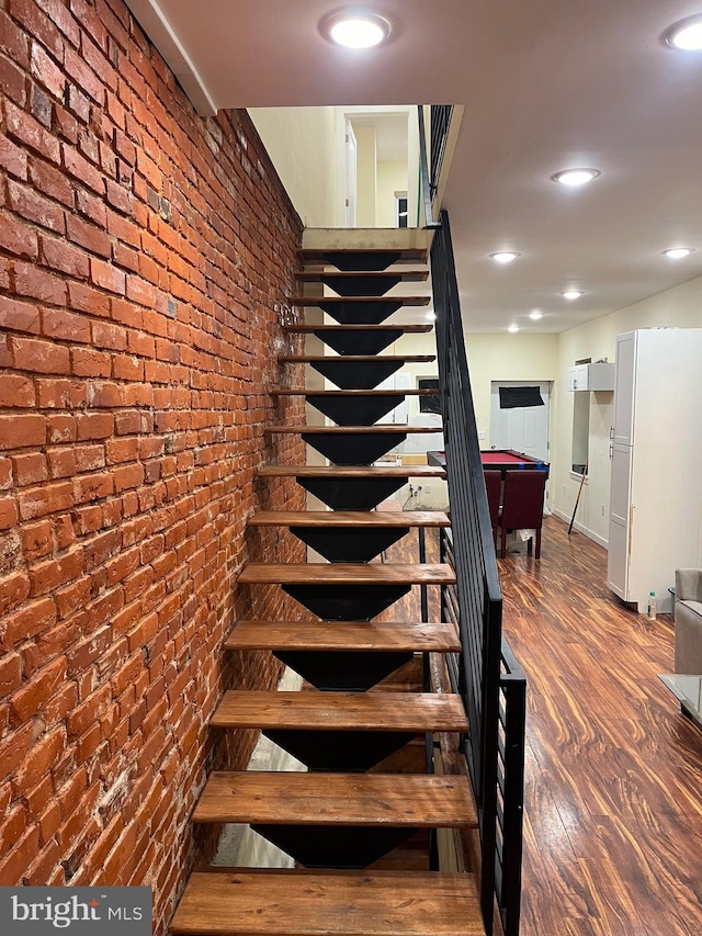 stairs with hardwood / wood-style flooring, pool table, and brick wall