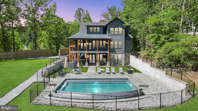 back of house at dusk with a patio area, a fenced backyard, stone siding, and a lawn