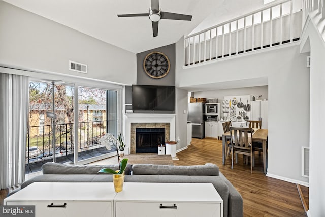 living room featuring high vaulted ceiling, a fireplace, visible vents, and wood finished floors