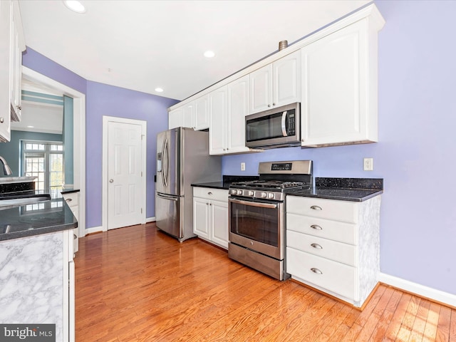 kitchen featuring appliances with stainless steel finishes, light hardwood / wood-style flooring, white cabinets, sink, and dark stone countertops