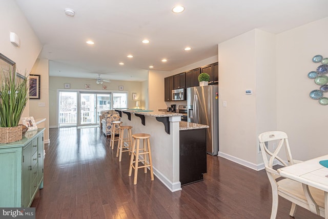 kitchen featuring stainless steel appliances, a center island, dark wood finished floors, light stone countertops, and a kitchen bar