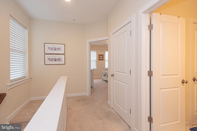 hall with light carpet, plenty of natural light, baseboards, and an upstairs landing