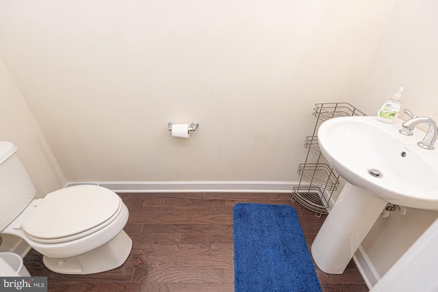 half bathroom featuring toilet, a sink, baseboards, and wood finished floors