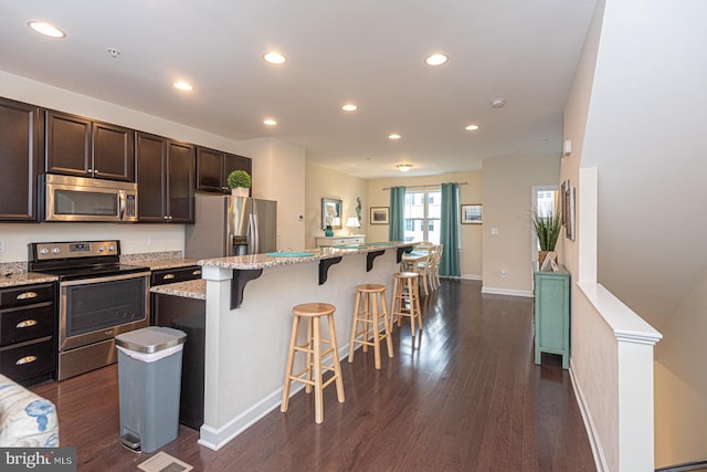 kitchen with stainless steel appliances, light stone counters, a kitchen bar, and a center island