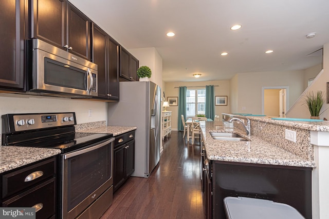 kitchen featuring stainless steel appliances, dark brown cabinetry, a sink, and light stone counters