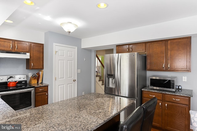 kitchen with stainless steel appliances, recessed lighting, brown cabinetry, light stone countertops, and under cabinet range hood