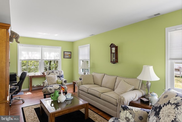 living area with baseboards, wood finished floors, visible vents, and a healthy amount of sunlight