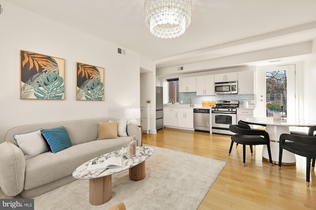 living area featuring light wood-type flooring, visible vents, and a chandelier