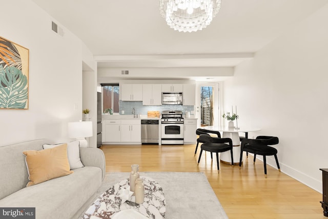 living area featuring baseboards, visible vents, an inviting chandelier, and light wood finished floors