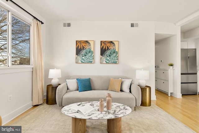 living room with baseboards, light wood finished floors, and visible vents