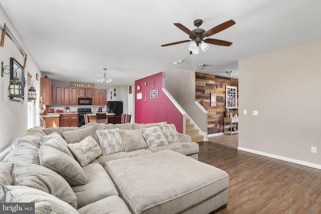 living area featuring dark wood-style floors, stairs, baseboards, and ceiling fan with notable chandelier