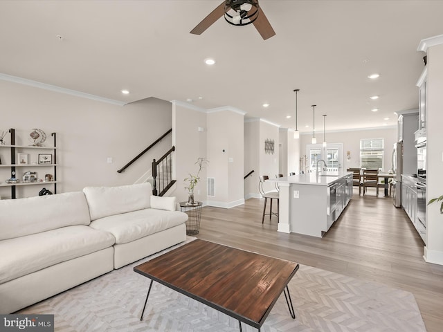 living area featuring light wood-style flooring, visible vents, ornamental molding, and recessed lighting