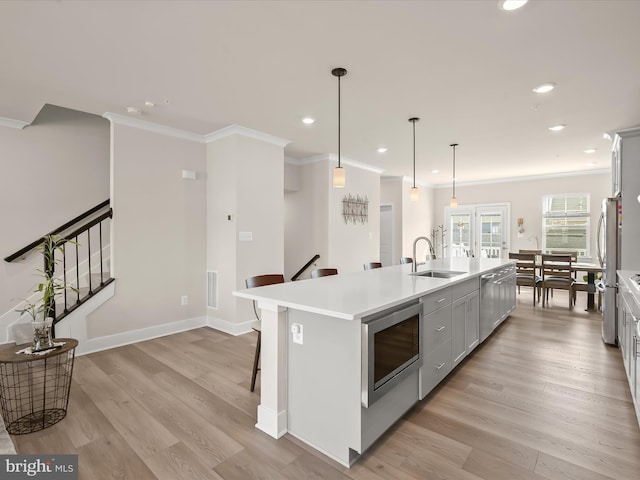 kitchen with light wood finished floors, stainless steel microwave, light countertops, and a sink