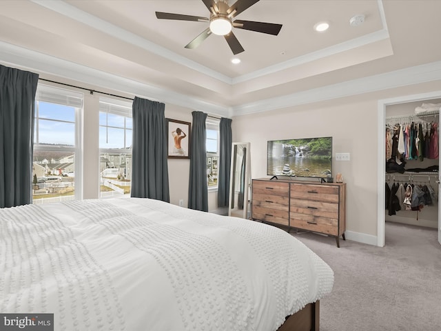 carpeted bedroom with a tray ceiling, a walk in closet, crown molding, a closet, and baseboards