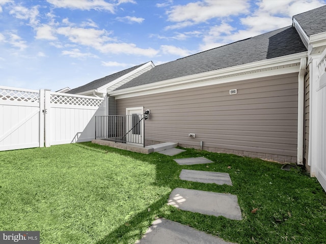 exterior space with a gate, roof with shingles, a lawn, and fence