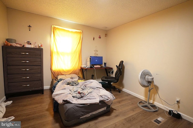 bedroom featuring a textured ceiling, baseboards, and wood finished floors