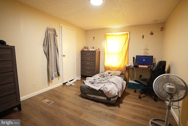 bedroom with baseboards, a textured ceiling, visible vents, and wood finished floors