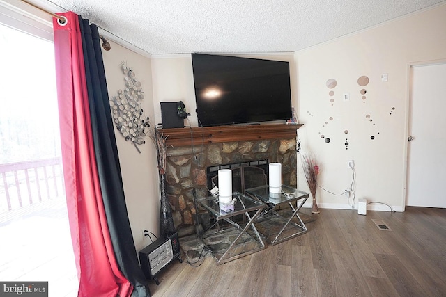 living room featuring a textured ceiling, a fireplace, wood finished floors, visible vents, and crown molding