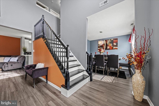 staircase featuring a high ceiling, wood finished floors, visible vents, and baseboards