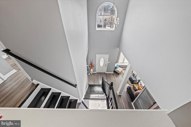 stairs featuring a notable chandelier, a high ceiling, baseboards, and wood finished floors