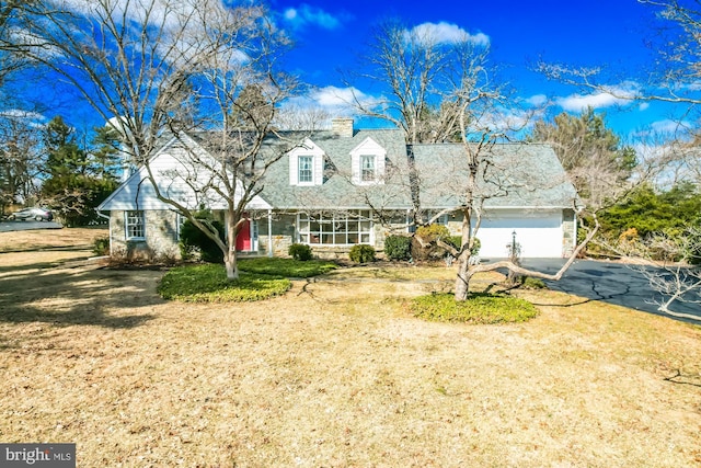 cape cod home featuring a chimney, an attached garage, a front yard, stone siding, and driveway