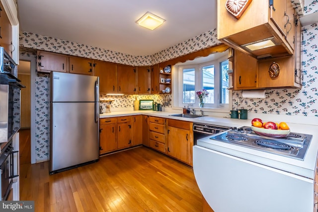 kitchen with light countertops, a sink, freestanding refrigerator, and brown cabinets